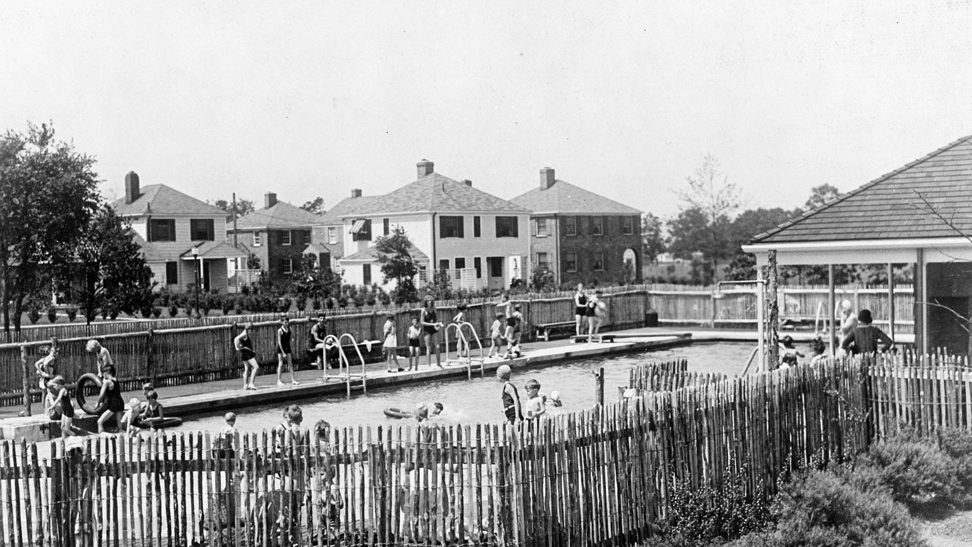 The Radburn pool. Wood-paling perimeter, houses behind. Stein and Wright designed the recreational program inside the superblock, not outside it.