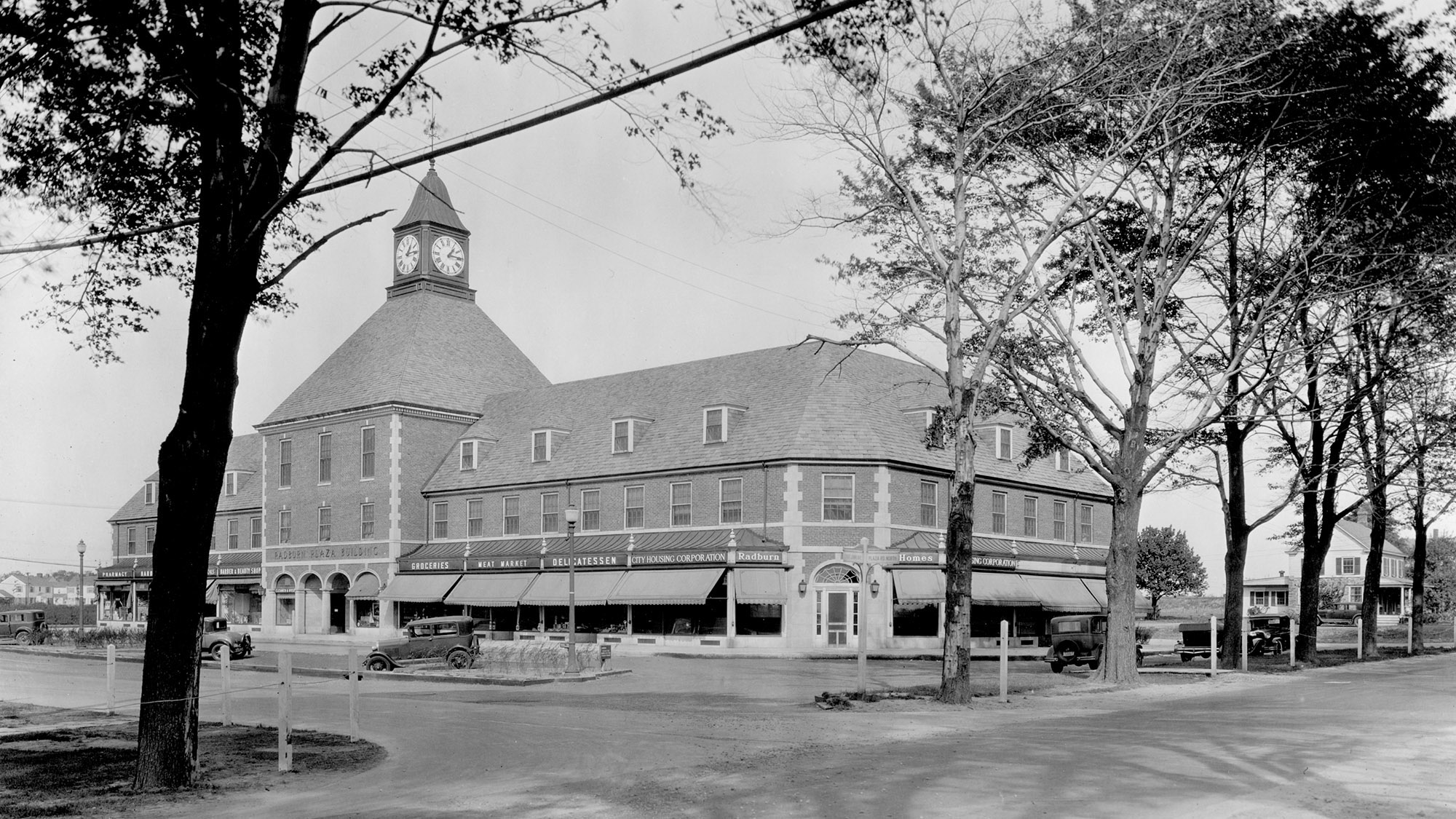 The Radburn Plaza Building, Frederick L. Ackerman, 1929. Shops below; Radburn Association offices, library, and meeting rooms above. The civic apparatus the buyer inherits with the deed.