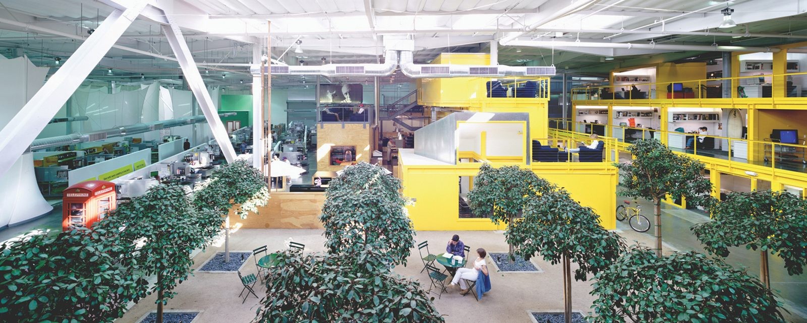 The indoor "Central Park" at TBWA\Chiat\Day. Outfitted with gravel, ficus trees, cafe chairs, and a red telephone box, the space drops the recognizable furniture of a public square directly onto an office floor plate to organically draw people together.